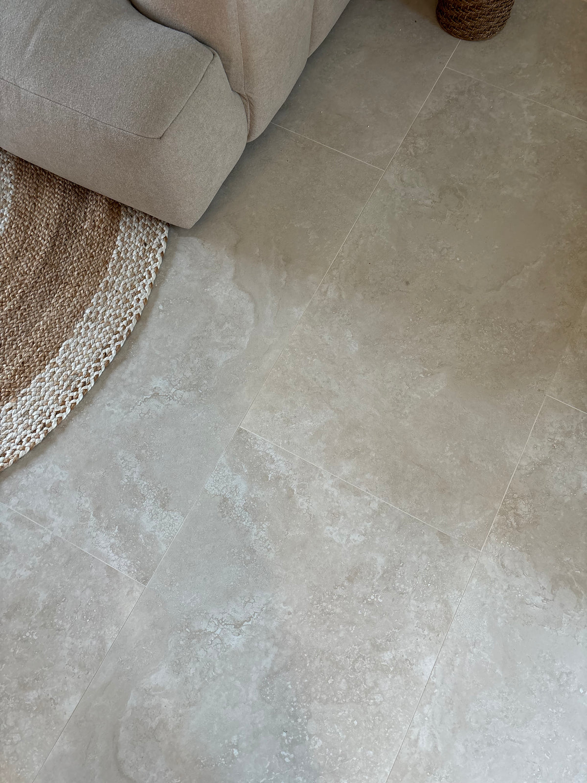 Beige stone-look floor tiles in a modern living room setting, shown next to a light beige sofa and a woven jute rug.