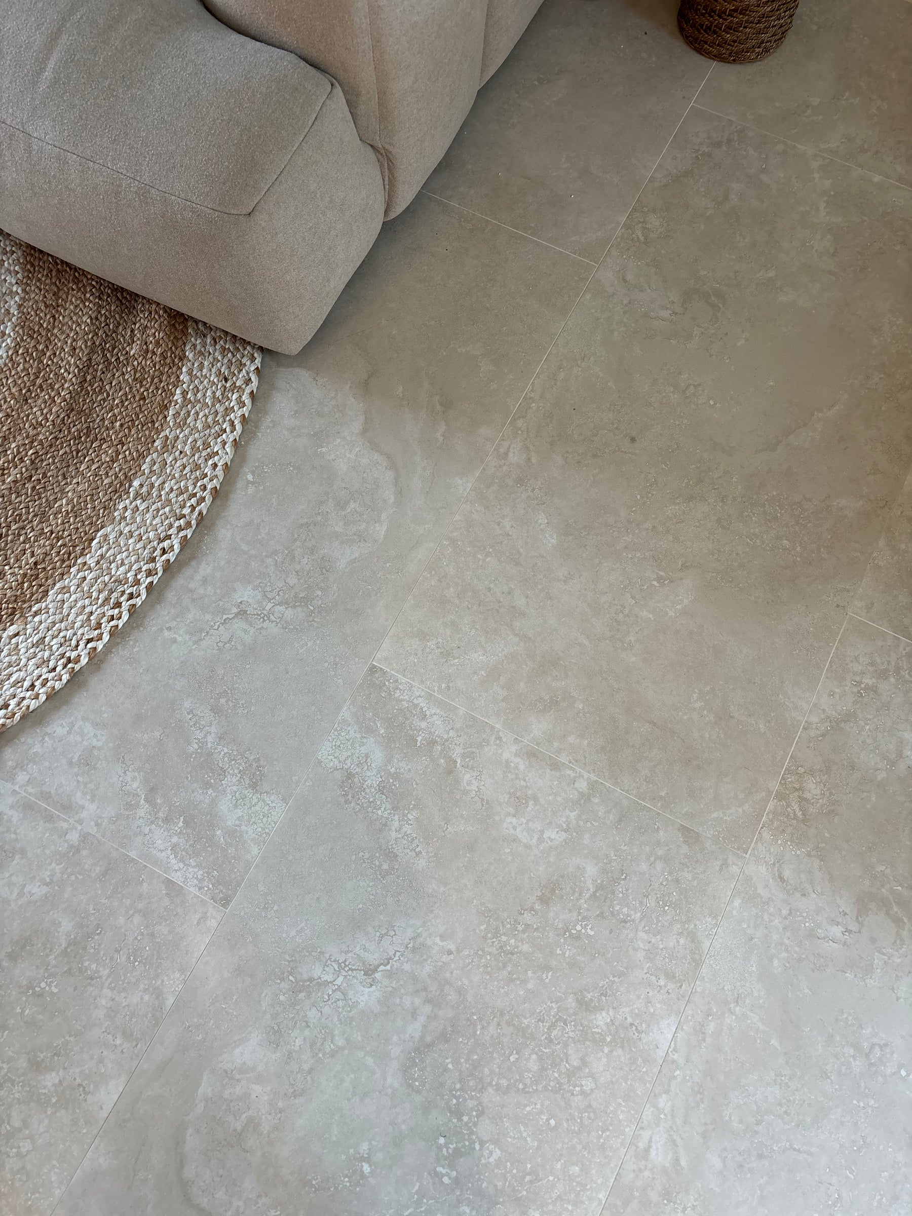 Beige stone-look floor tiles in a modern living room setting, shown next to a light beige sofa and a woven jute rug.