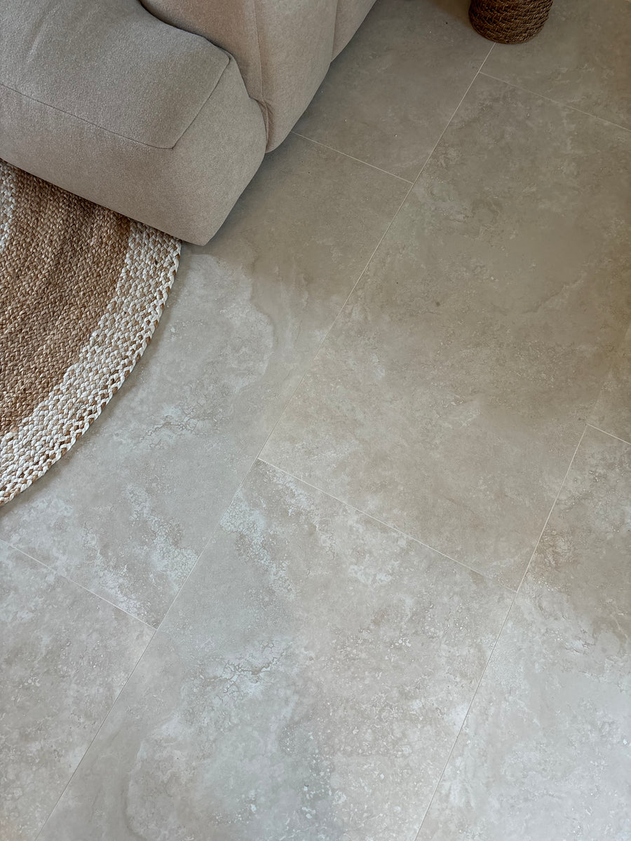 Beige stone-look floor tiles in a modern living room setting, shown next to a light beige sofa and a woven jute rug.